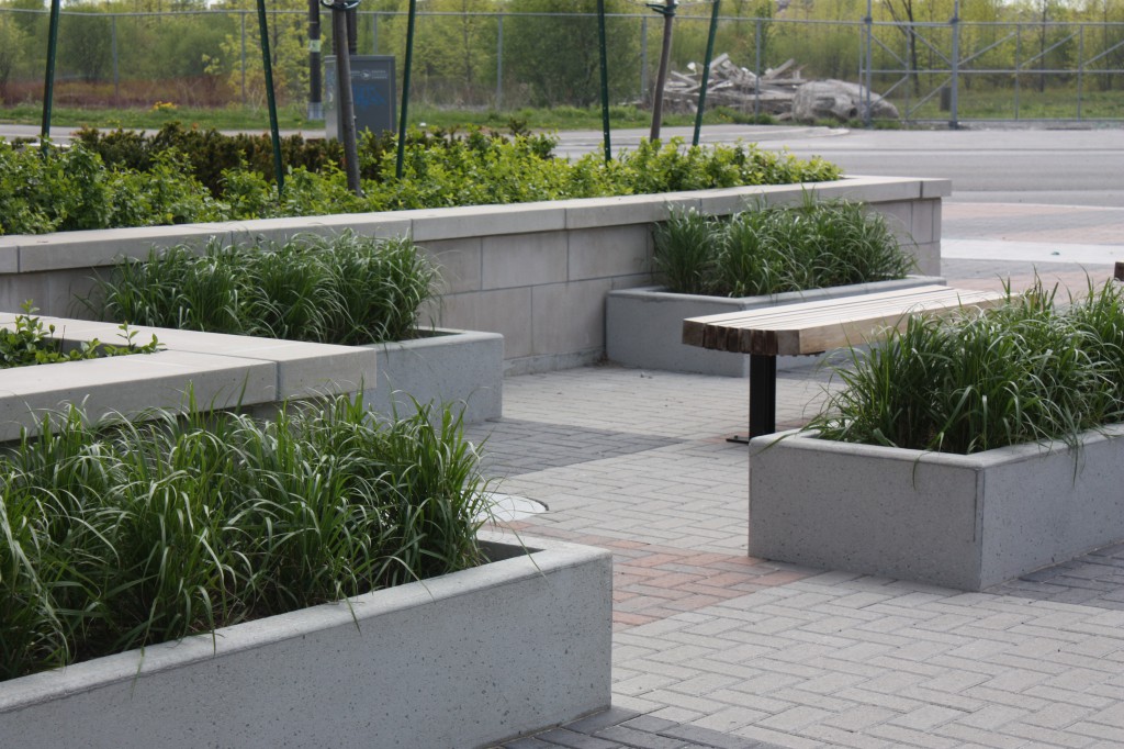 The Entry Piazza The entry plaza doubles as a public parkette.  Modular planters are used to create a rhythm of structure and textural variations to the ground plane.  Seating disbursed throughout is inviting.